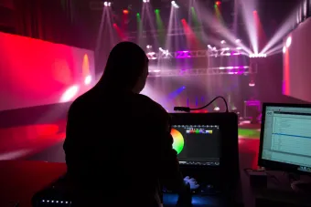 pink, blue and yellow concert lighting with a woman's silhouette in the foreground at the programming board 