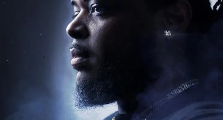 Portrait of Andrew Augustin looking to the side, wearing layered gold necklaces, with a misty background and soft lighting.